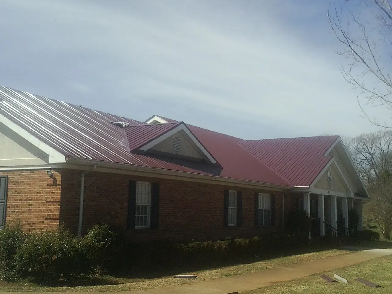 Red metal roof with gabled entries on a long brick building, from a Hail Damage Roof Repair job in Idaho Falls