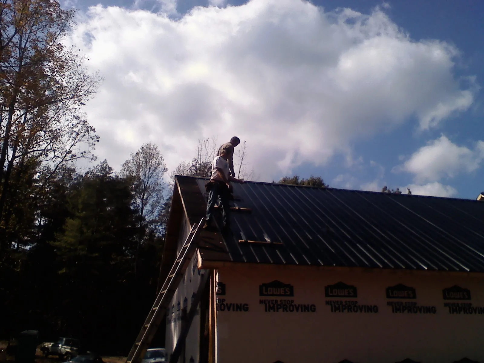 Roofer fastening dark metal panels high against a cloudy sky, from a Roof Inspection job in Idaho Falls