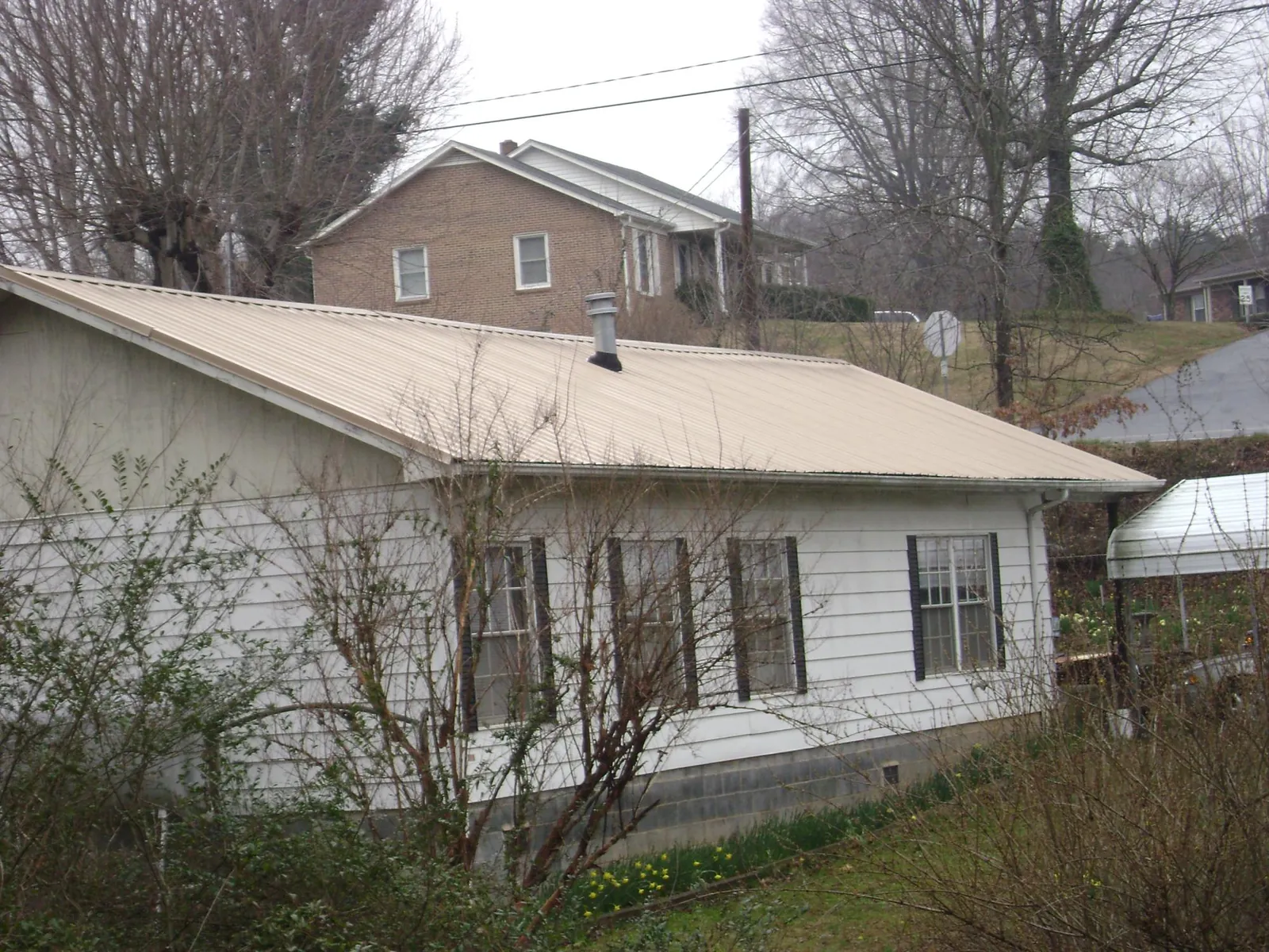 Tan metal roof on a white sided house set into a hillside — Commercial Roofing by Roofing Brothers in Idaho Falls